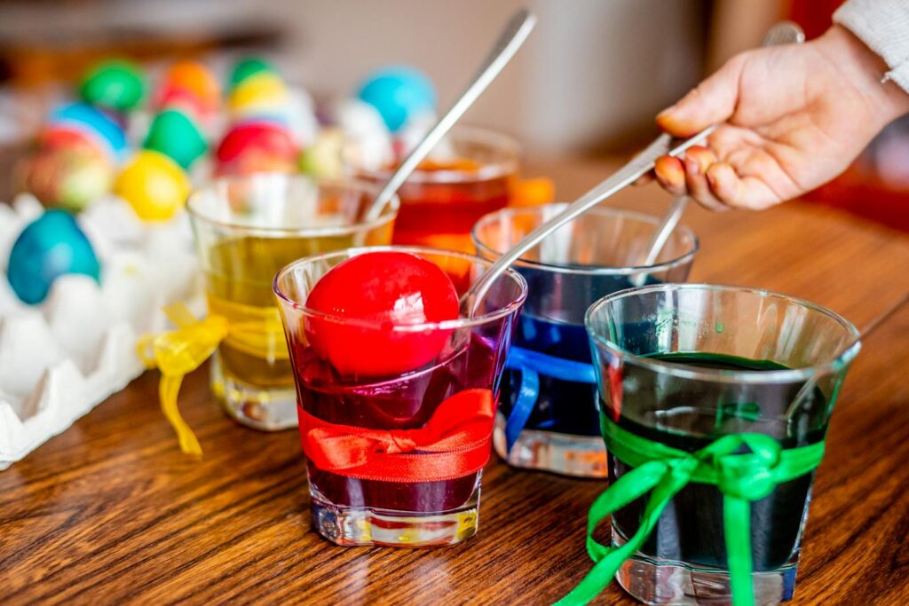Close-up of vibrant Easter eggs being dyed in colorful glass jars with a hand holding a spoon.