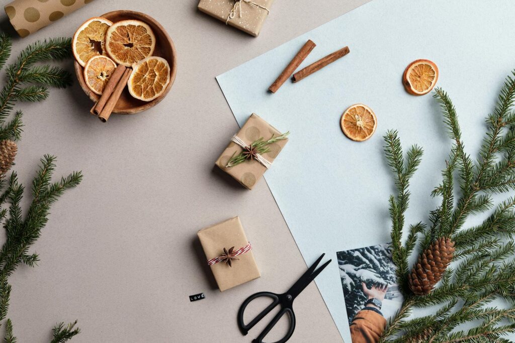 Top view of a festive flatlay featuring gifts, dried orange slices, pine branches, and cinnamon sticks.