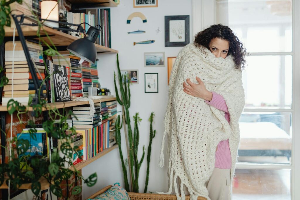 A woman warmly wrapped in a thick blanket, enjoying relaxation in her cozy, book-filled home.